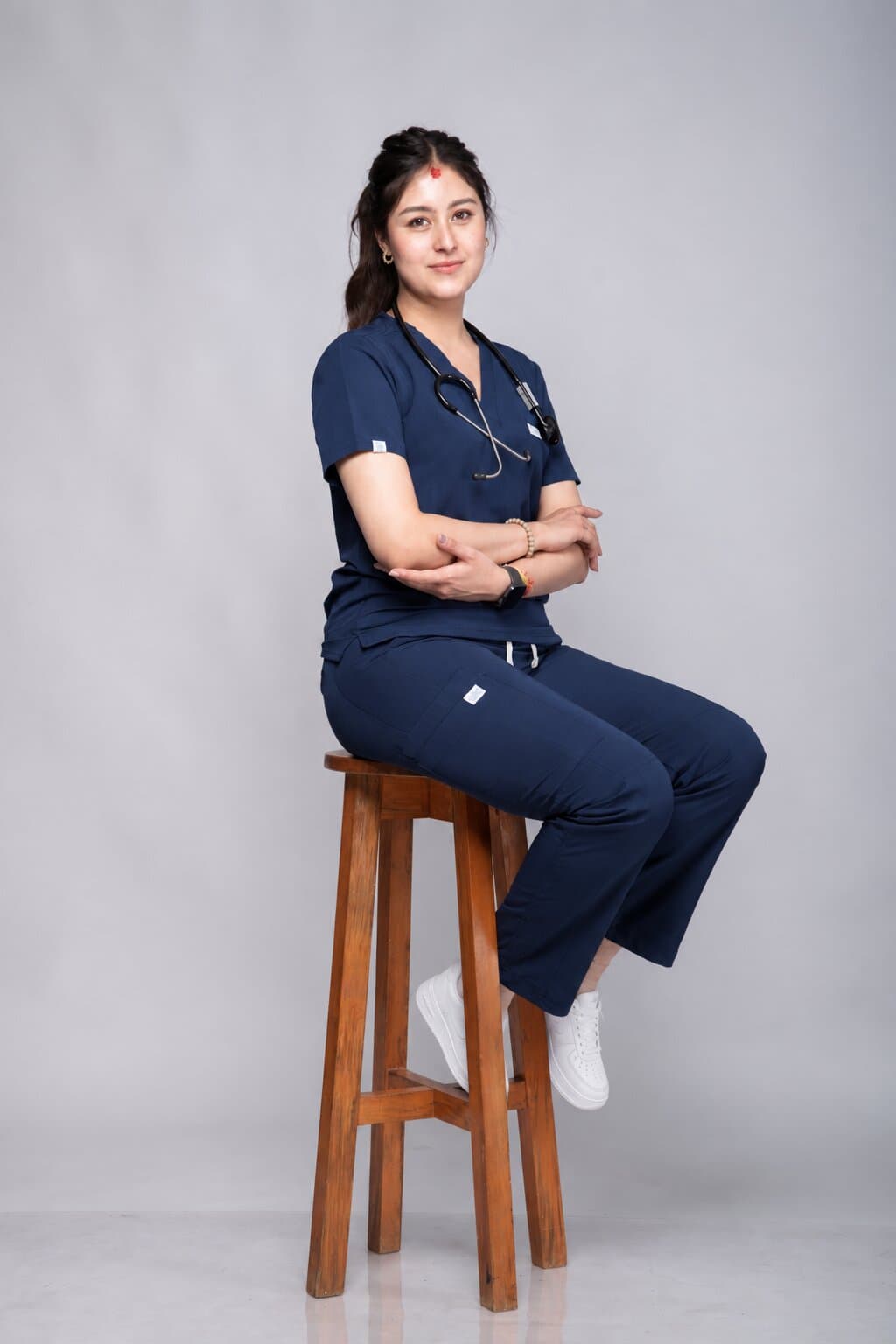 Nurse in a navy Medisewa scrub set sitting on a wooden stool